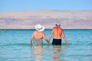 Older couple on holiday wading in the sea holding hands enjoying an active and healthy life